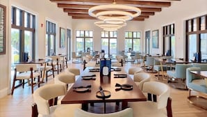 Un amplio comedor con mesas y sillas largas, ventanas grandes y techo de madera.