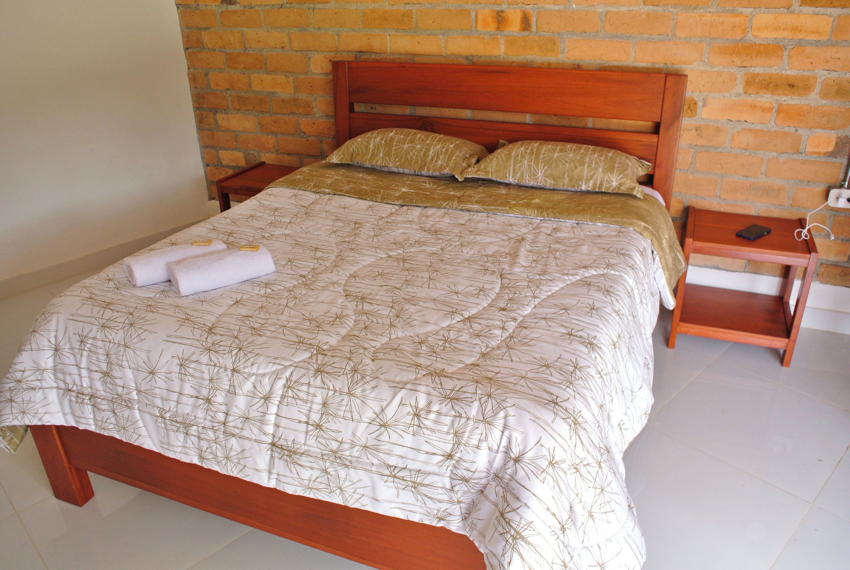 Una cama bien hecha con una colcha estampada, dos almohadas y dos toallas dobladas a un lado.