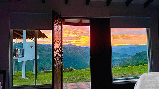 Habitación con un amplio ventanal que ofrece vistas a un paisaje montañoso al atardecer.