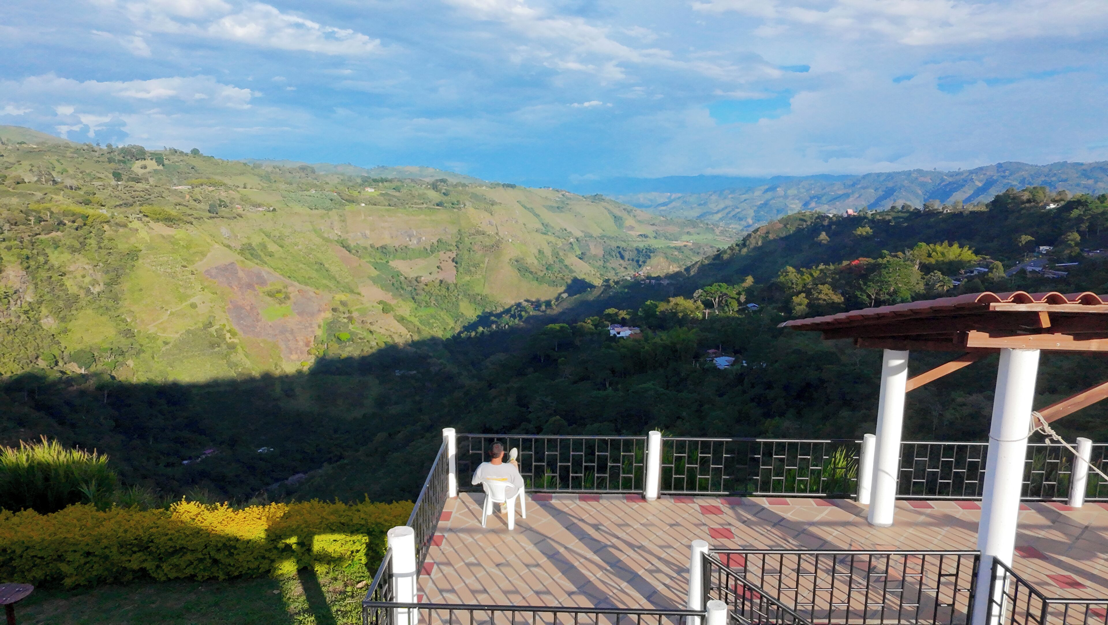A terrace with a view of a valley, a person sitting, and a pergola structure.