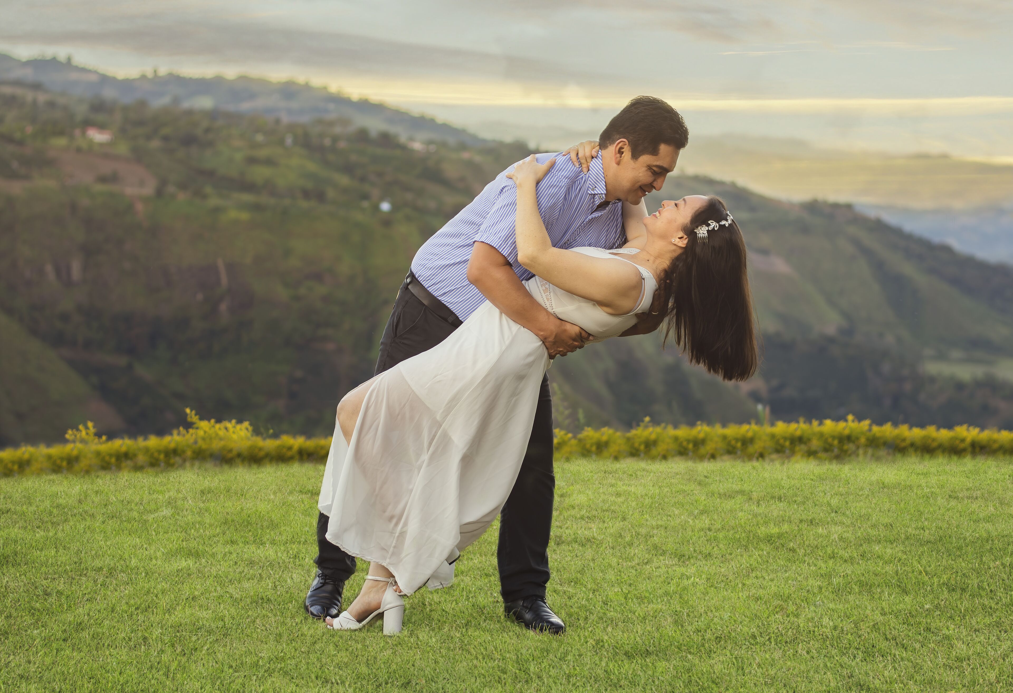 A couple embracing in a grassy field with a mountainous backdrop.