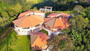 Una casa grande de varios pisos con un patio central, rodeada de exuberante vegetación y colinas.