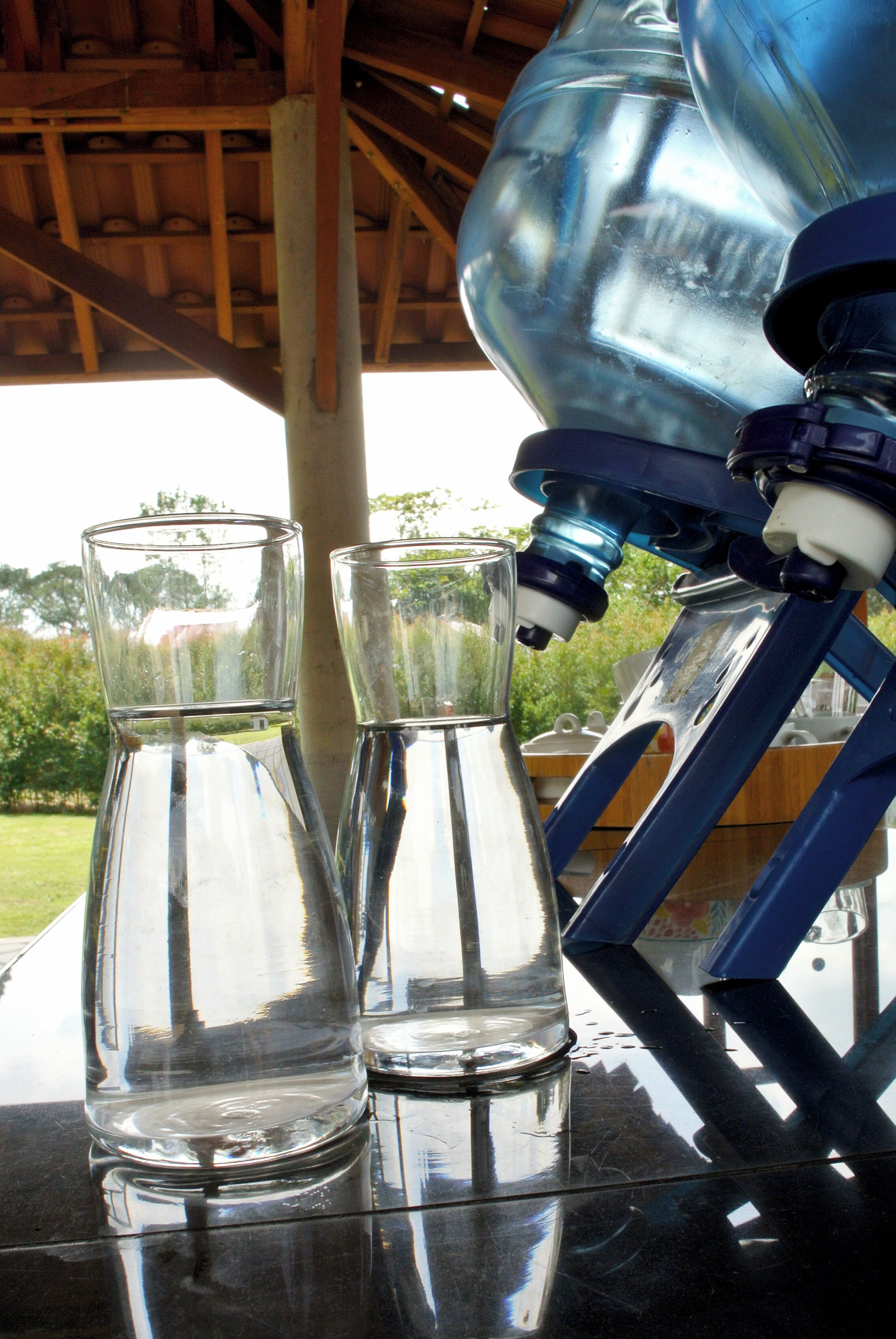 Two clear glass bottles and a blue water dispenser on a reflective surface.