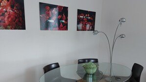 A modern dining area with a glass table surrounded by four chairs, one red and three brown. Three framed artworks are hung on the wall above the table. - Charmante Maison de Village , Tout à Pied, Commerces et Plage à 5 mn (Perros-Guirec)
