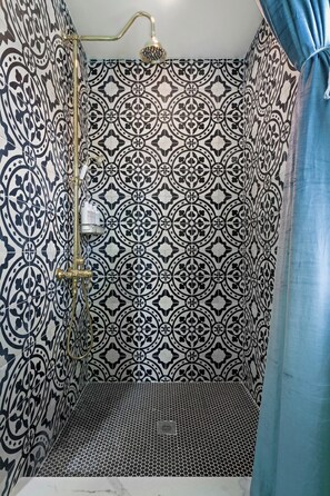 A bathroom with patterned tiles, a shower with a gold faucet, and a blue curtain.