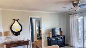 Un saló amb un sofà, una televisió sobre un moble, un ventilador de sostre i una porta que dona a una altra habitació.