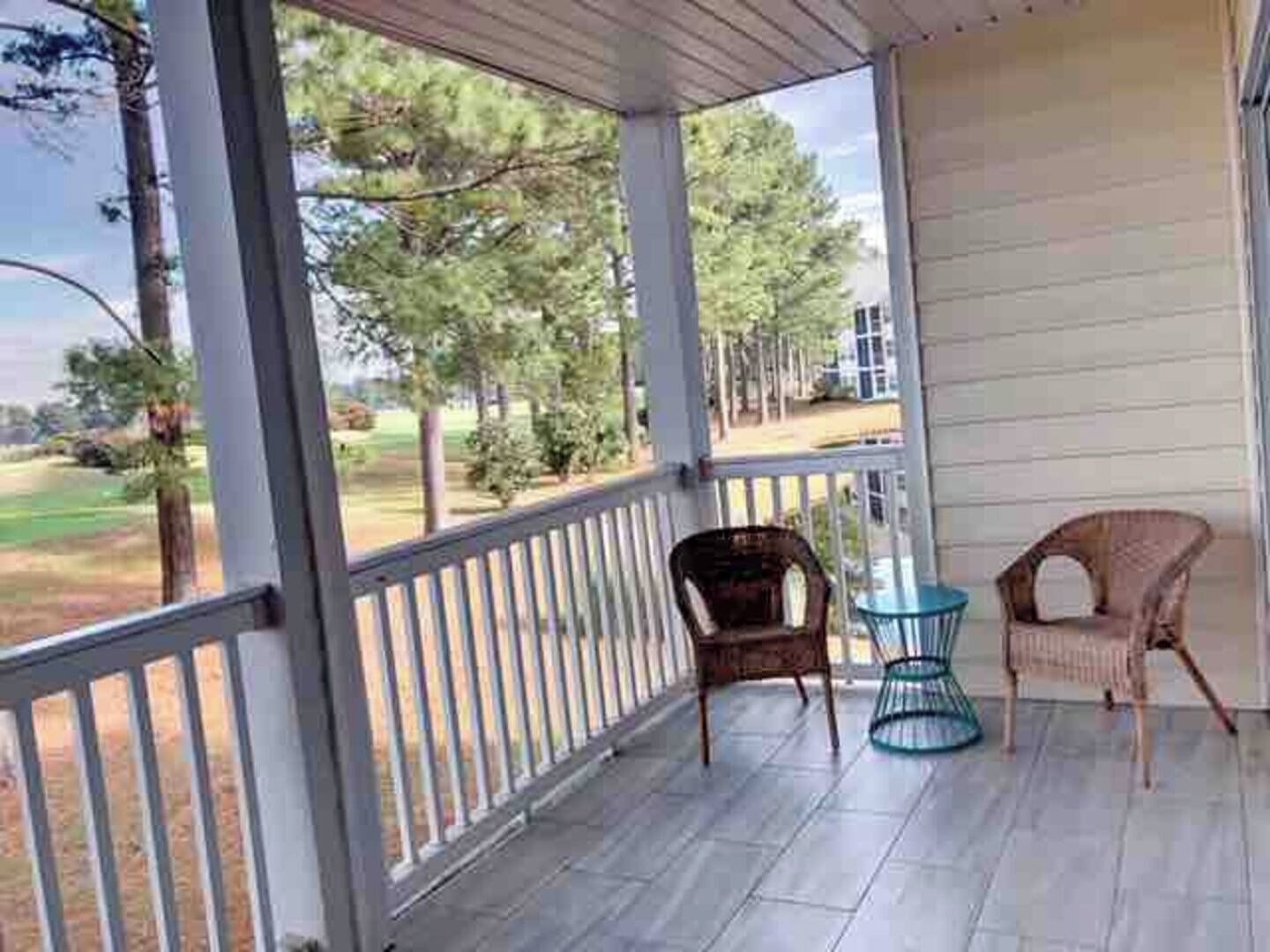 Un porche abrité, doté d’une balustrade, de deux fauteuils en osier et d’une petite table.