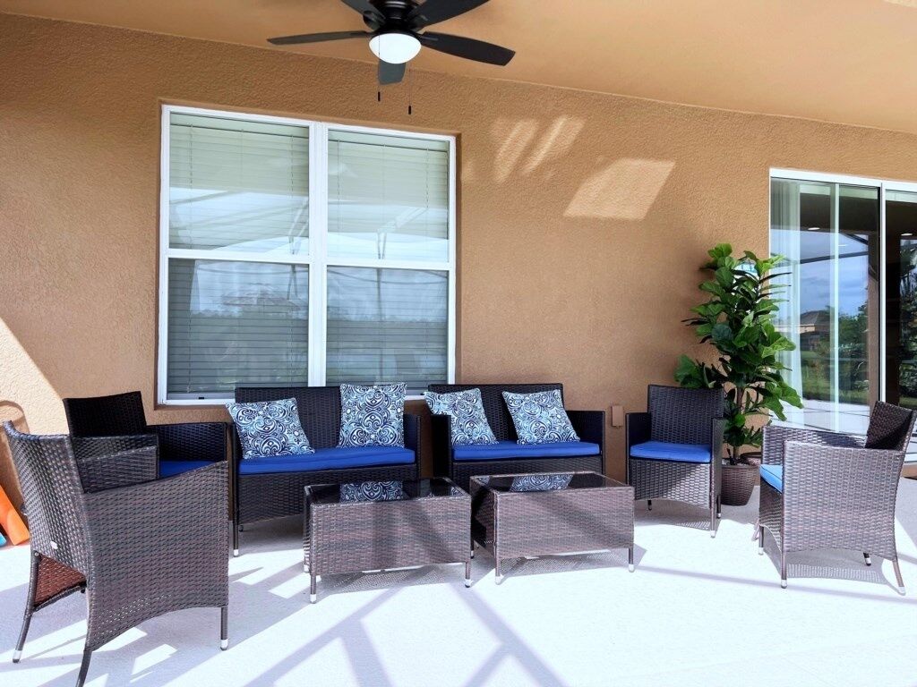 An outdoor patio with wicker furniture, a ceiling fan, and large windows.