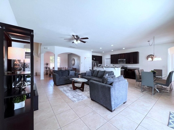 A modern living room with grey sofas, a coffee table, and a dining area with chairs. - Cozy Family Friendly Pool Home With Game Room-227y 5 Bedroom Home by RedAwning (Davenport)