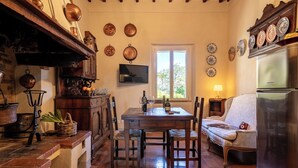 A cozy kitchen with a wooden table, chairs, and a refrigerator. There are copper pots on the wall and a television above the table. - Monticchiello (Pienza)