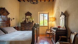 A bedroom with a wooden bed, dresser, and chair, a window with a view, and a chandelier. - Monticchiello (Pienza)