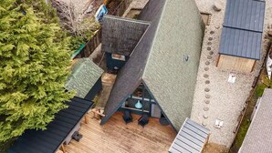 A modern house with a sloped roof, a deck with outdoor furniture, and a view of a body of water. - NEW! A Frame Over Water - Sauna, Hot Tub, Views (Tahuya)