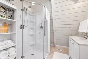 A modern bathroom with a glass-enclosed shower, white cabinetry, and a wooden shelf with towels. - NEW! A Frame Over Water - Sauna, Hot Tub, Views (Tahuya)