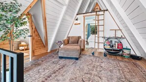 A cozy attic room with a loft bed, a plush sofa, and a ladder leading to a lofted sleeping area. - NEW! A Frame Over Water - Sauna, Hot Tub, Views (Tahuya)