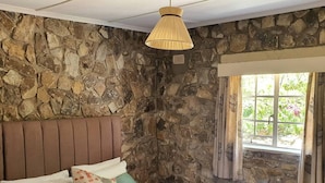 Une chambre avec un mur en pierre, une tête de lit en bois et une fenêtre avec des rideaux.
