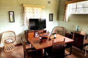 Un comedor con una mesa de madera, sillas, un televisor y una ventana con cortinas.