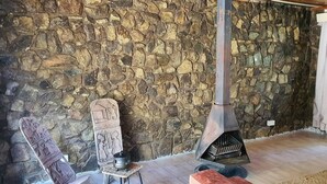 Une pièce aux murs de pierre, dotée d’une cheminée, d’un banc en bois et d’un coin salon avec des coussins rouges.