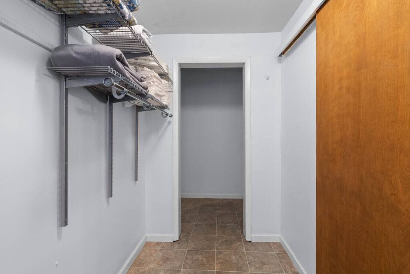 Un couloir étroit, avec une porte en bois sur la droite et un présentoir en métal contenant des serviettes sur la gauche.