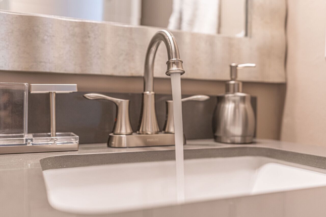 A modern bathroom sink with a single faucet, a soap dispenser, and a clear glass soap dish.