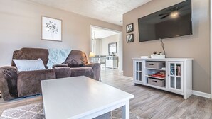 Un salon avec un canapé marron, une table basse blanche et un téléviseur fixé au mur.