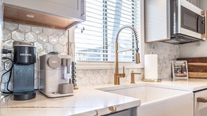 Une cuisine moderne équipée d’une machine à café Keurig, d’une machine à café Nespresso, d’un robinet doré et d’un four à micro-ondes placé au-dessus du plan de travail.