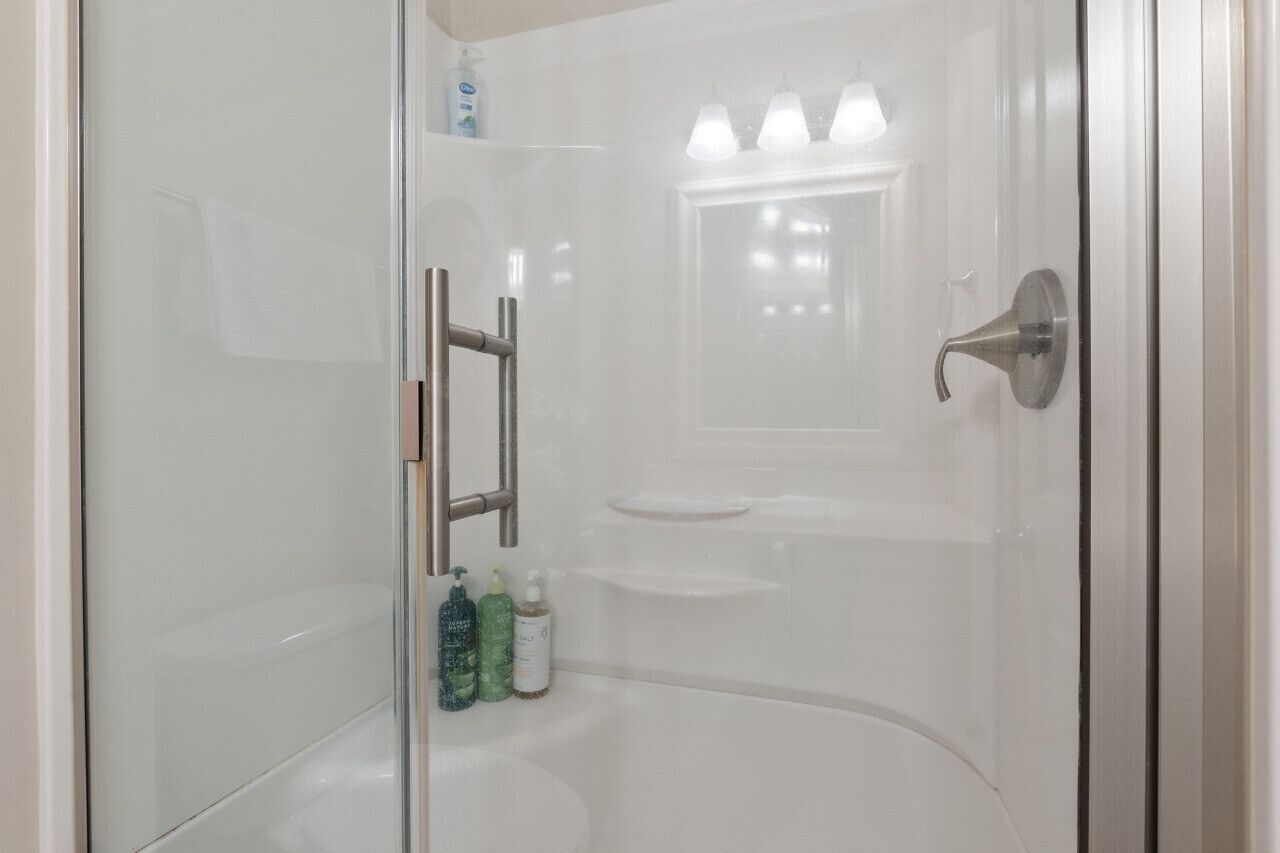 A glass-enclosed shower stall with a handheld showerhead, a glass door, and a small shelf with toiletries.