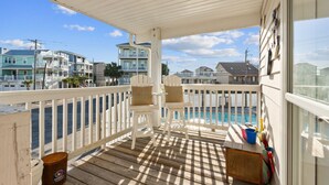 A wooden deck with white railings, two white chairs with cushions, a small table, and a bucket. - Canal-Front Townhome w/ Private Boat Slip, Pool & Beach Access (Carolina Beach)