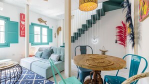 A modern living room with teal accents, a staircase, and a dining area with a round wooden table. - Petite Maison Lili (Málaga)