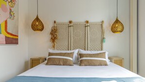 A neatly made bed with two pillows, a blue throw blanket, and two bedside tables with lamps. - Petite Maison Lili (Málaga)