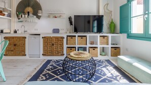 A modern kitchen with white cabinetry, a large TV, and a teal window. - Petite Maison Lili (Málaga)