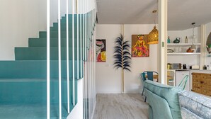 A staircase with teal steps leading to a room with a dining area, a large plant, and a colorful painting. - Petite Maison Lili (Málaga)