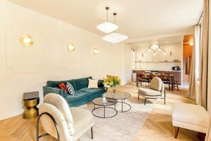Ein modernes Wohnzimmer mit einer Couch, Sesseln, einem Couchtisch und einem Essbereich im Hintergrund.
