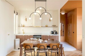 Una cocina moderna con zona de comedor, que incluye una isla central, iluminación colgante y un horno empotrado.