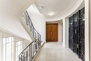 Ein geräumiger Flur mit einer geschwungenen Treppe, einer Holztür und einem Metallgitter.