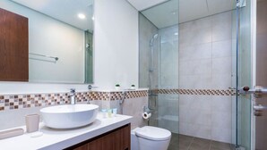 Un baño moderno con un lavabo blanco grande, un inodoro y una zona de ducha con mampara de vidrio.