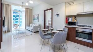 Una sala moderna con una mesa de comedor de vidrio, sillas grises, un sofá y un amplio ventanal con cortinas.