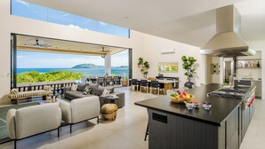 A modern open-plan living area with a kitchen, large windows overlooking the sea, and a dining area. - Staffed Luxury Oceanview Villa w/ golfcart, jacuzzi, infinity pool &breakfast (Playa Tamarindo)