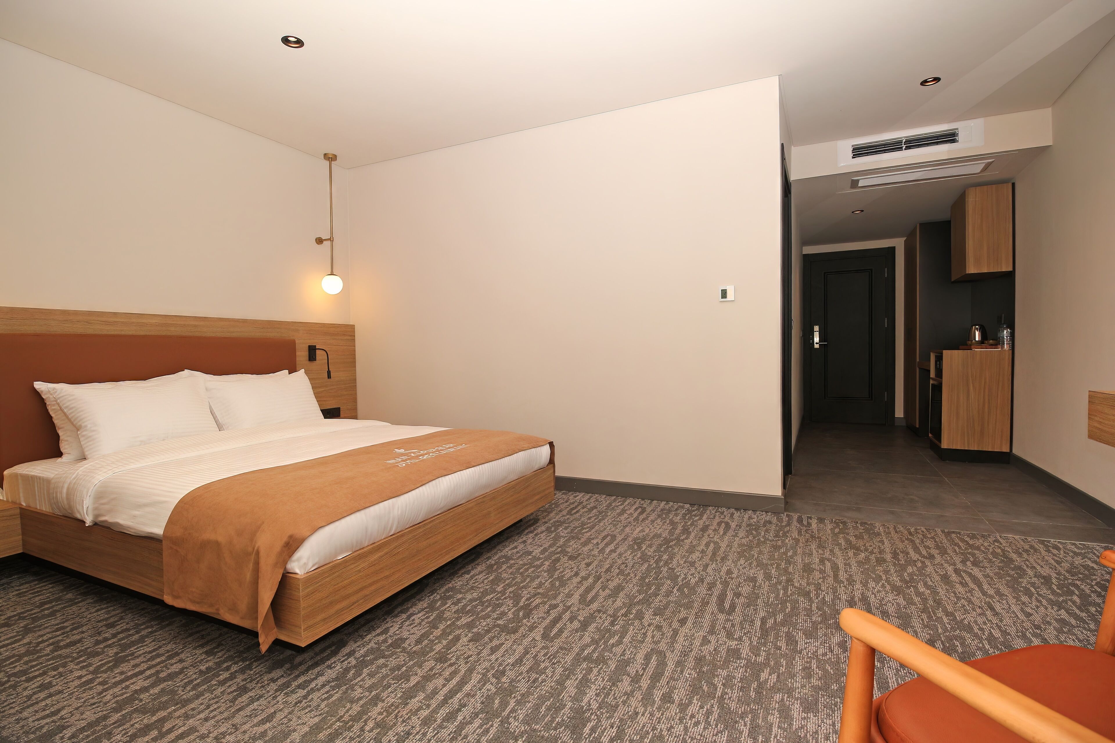 A hotel room with a bed, a chair, a desk, and a kitchenette.