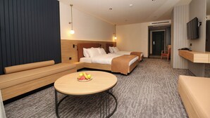 Une chambre d’hôtel moderne équipée d’un lit, d’un canapé, d’une petite table avec des fruits et d’une télévision.