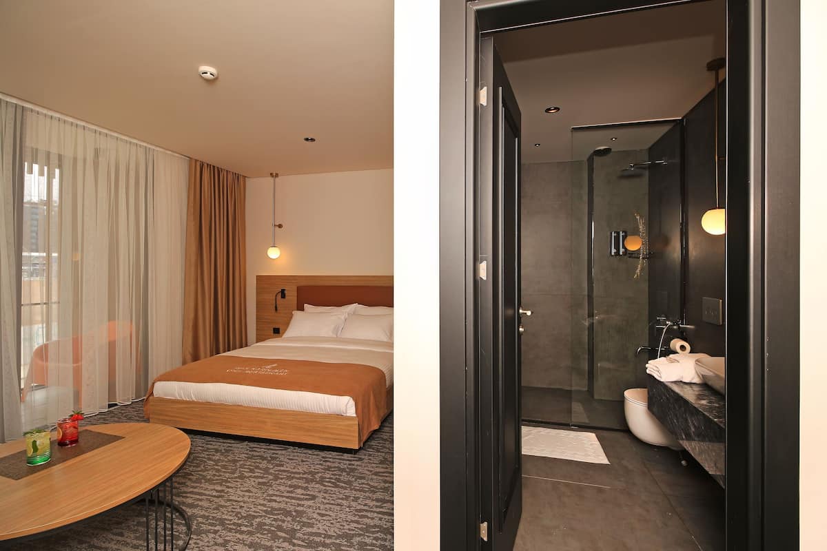 A hotel room with a bed, bedside table, and a bathroom with a shower and toilet.