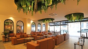 Un espace intérieur spacieux avec de nombreux canapés et tables, de grandes fenêtres et des plantes suspendues.