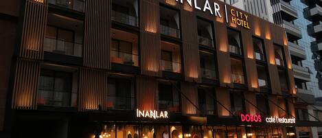 A hotel with a modern facade, featuring vertical wooden slats and illuminated signage.