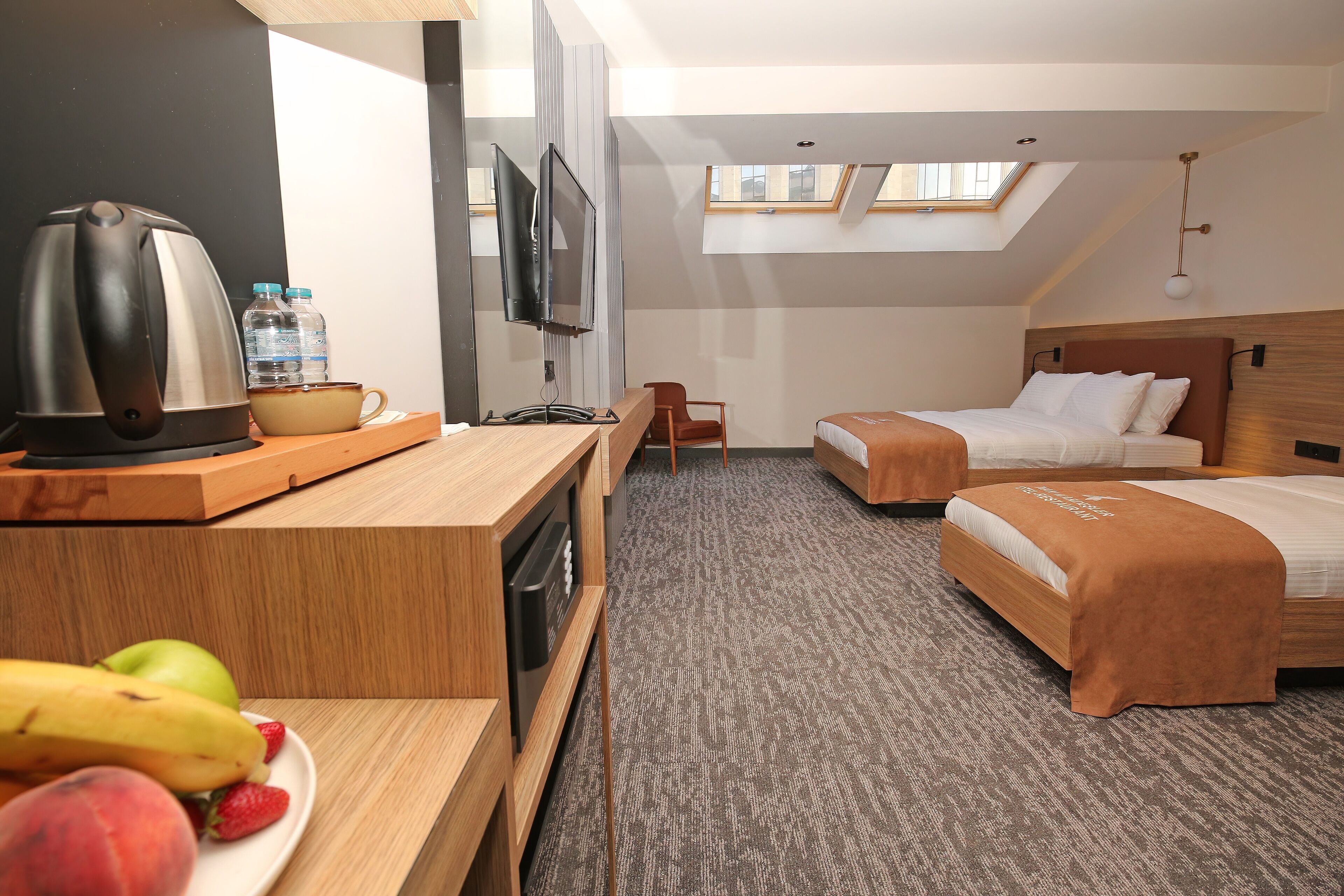 Quarto de hotel com cozinha compacta, duas camas, televisão e claraboia.