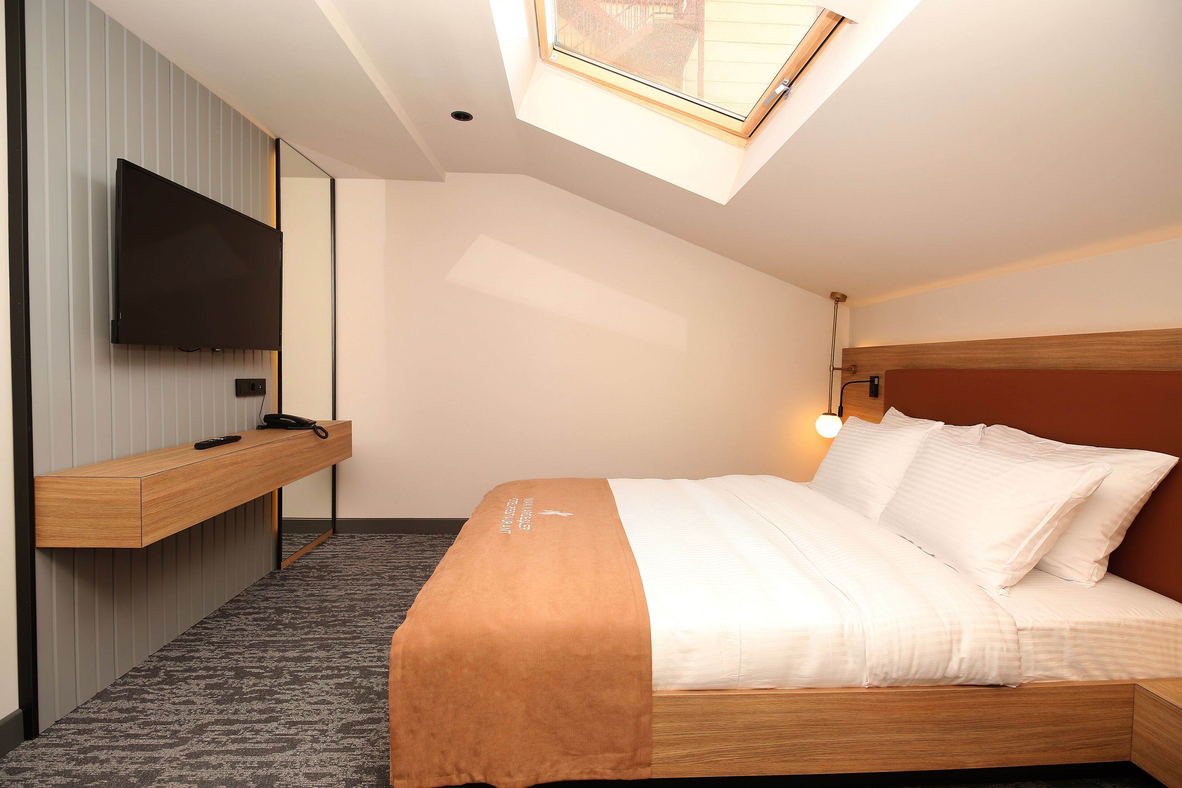 Une chambre d’hôtel moderne équipée d’un lit, d’un téléviseur fixé au mur, d’une table de chevet et d’une lucarne.