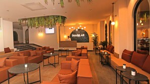 Un espace de détente moderne avec des canapés orange, des tables rondes et des plantes suspendues.