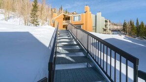 Una scala coperta di neve che conduce a un edificio con balconi, circondato da alberi.