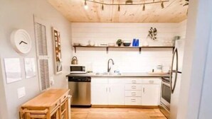Una cucina compatta con pavimento in legno, forno a incasso, lavello e un piccolo angolo ristoro con tavolo in legno.