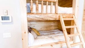 Un letto a castello con una scala in legno, un piccolo ripiano e una presa elettrica sulla parete.