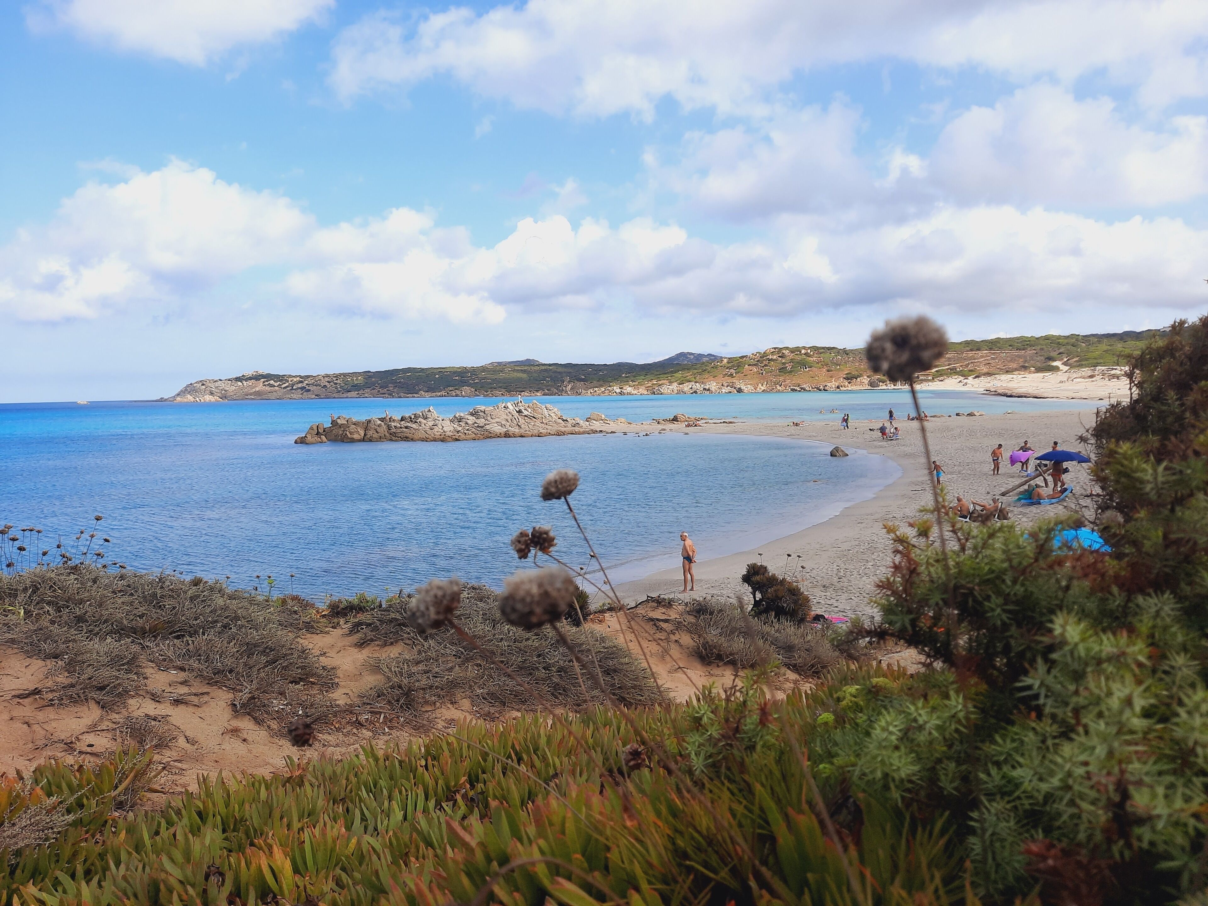 A beach with clear blue water, rocky outcrops, and people enjoying the sun.