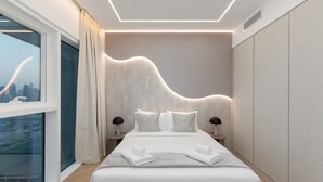 Una camera da letto moderna con un'ampia finestra, un letto con lenzuola bianche e un originale design della parete ondulata.